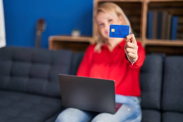 年轻的金发女人坐在家里的沙发上 用笔记本电脑和信用卡 — 图库照片
