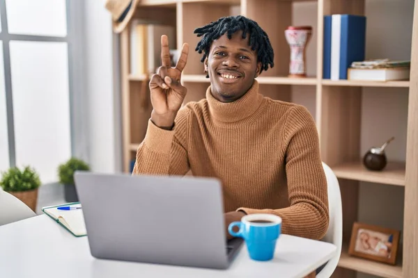 自信を持って幸せな笑みを浮かべている間 コンピュータのラップトップを表示し 指の数2を指差す使用して働いている恐ろしいロックを持つ若いアフリカの男 — ストック写真