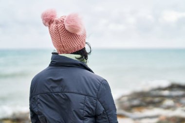 Young beautiful hispanic woman standing on back view at seaside