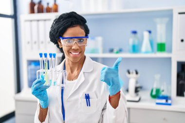 Orta yaşlı İspanyol bir kadın, bilim adamının laboratuvarında çalışıyor mutlu ve pozitif gülümsüyor, başparmağı mükemmel ve onay işareti yapıyor. 