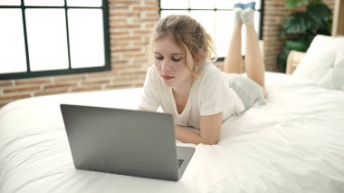 Yatak odasında dizüstü bilgisayar kullanan genç sarışın kadın.