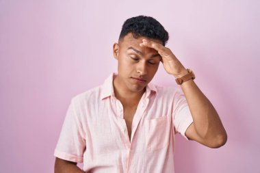 Young hispanic man standing over pink background worried and stressed about a problem with hand on forehead, nervous and anxious for crisis 