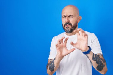 Mavi arka planda duran İspanyol dövmeli adam tiksindirici bir ifade takınıyor ve tiksindirici bir yüz ifadesi takınıyor.. 