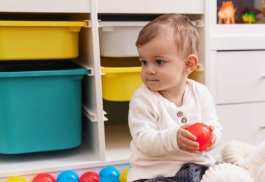Anaokulunda yerde taşaklarıyla oynayan sevimli beyaz çocuk.