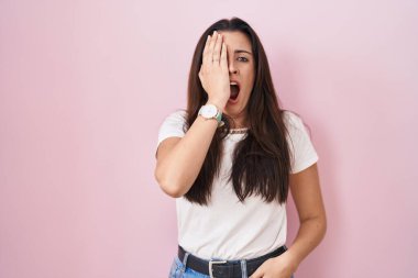 Genç esmer kadın pembe arka planda duruyor. Yarı yüz, göz ve ağzı elle kapatmaktan yorulmuş. Yüzüm acıyor.. 