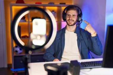 Sakallı İspanyol bir adam akıllı telefonuyla video kaydı yapıyor. Mutlu bir gülümsemeyle eli ve parmağı ile işaret ediyor. 