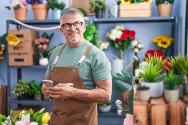 Çiçekçinin önünde duran akıllı telefonu kullanan kır saçlı bir çiçekçi.