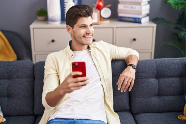 Evdeki kanepede oturan, akıllı telefon kullanan genç bir İspanyol.