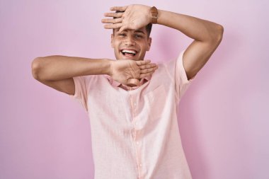 Pembe arka planda duran genç, İspanyol bir adam gülümseyen, gülümseyen ve elleri havada bir yuhalama oyunu oynayan. Şaşırdım ve çıktım. 