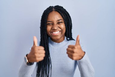 African american woman standing over blue background success sign doing positive gesture with hand, thumbs up smiling and happy. cheerful expression and winner gesture. 