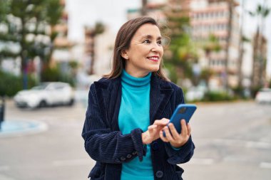 Sokakta akıllı telefon kullanan orta yaşlı bir iş kadını.