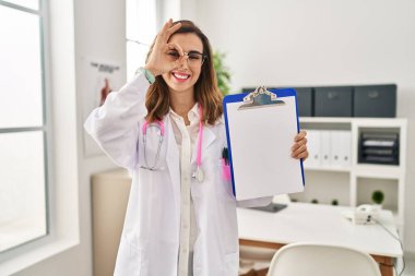 Genç doktor kadın elinde bir pano tutarak gülümsüyor. Mutluluktan gülümsüyor. 