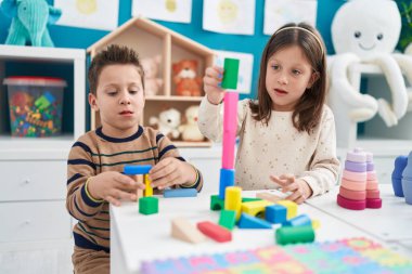 Anaokulundaki masada oturan sevimli kız ve oğlan inşaat bloklarıyla oynuyorlar.