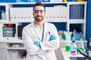 Genç İspanyol bilim adamı, laboratuvarda kendine güvenen, kollarını kavuşturup gülümsüyor.