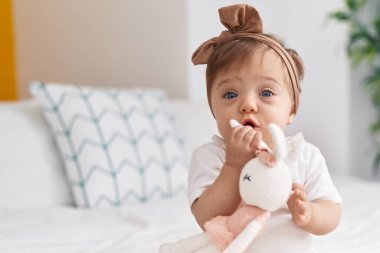 Sevimli beyaz bebek yatak odasında bebek ısırıyor.