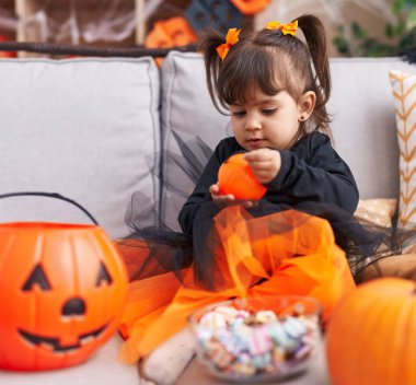 Adorable hispanic girl wearing halloween costume holding pumpkin basket at home