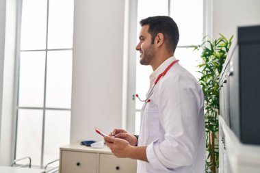 Klinikte dokunmatik ped kullanan İspanyol doktor üniforması giyen genç adam.