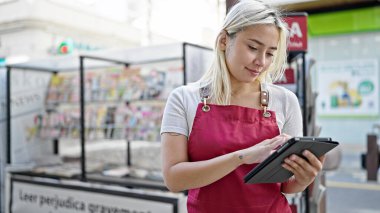 Gazetecide dokunmatik ped kullanan önlük giyen genç, güzel bir İspanyol kadın.