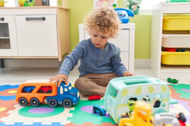 Sevimli sarışın çocuk arabalarla oynuyor. Anaokulunda yerde oturuyor.