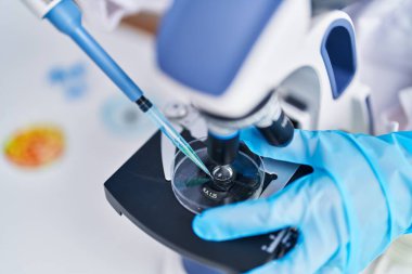 Laboratuvarda mikroskop kullanarak numuneye sıvı döken genç bir bilim kadını.