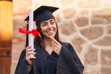 Mezuniyet üniforması giyen genç İspanyol kadın üniversiteyi parmağıyla işaret ediyor.