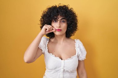 Sarı arka planda duran kıvırcık saçlı, genç esmer kadın ağzı ve dudakları parmaklarıyla fermuar gibi kapalı. gizli ve sessiz, tabu konuşması 