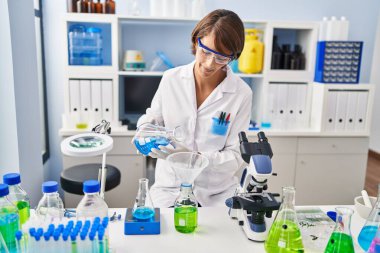 Genç ve güzel İspanyol bilim kadını laboratuarda şişenin üzerine sıvı döküyor.