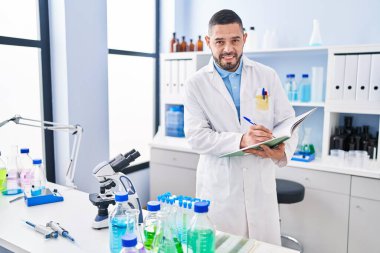 Genç Latin bilim adamı gülümsüyor. Laboratuvarda deftere kendinden emin bir yazı yazıyor.