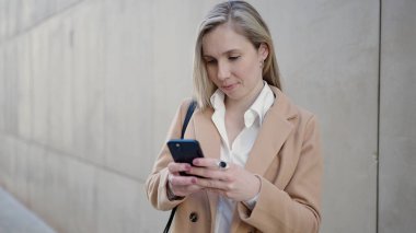 Sokakta duran akıllı telefonu kullanan genç sarışın kadın.