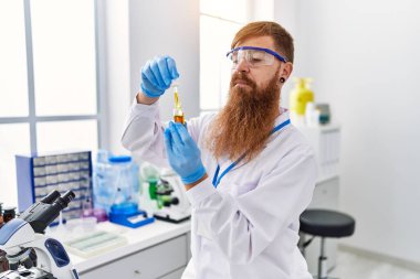 Bilim adamı üniforması giyen genç kızıl adam laboratuvarda tepkili duruyor.