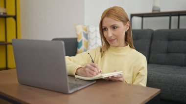 Evde dizüstü bilgisayar kullanan genç sarışın kadın.