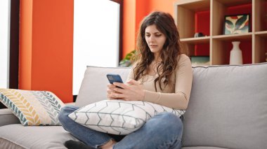 Genç ve güzel İspanyol kadın evde üzgün akıllı telefon kullanıyor.