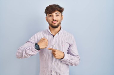 Mavi arka planda duran sakallı bir Arap, acele ederek saati, sabırsızlığı ve rahat bir ifadeyle kameraya bakmayı işaret ediyor. 