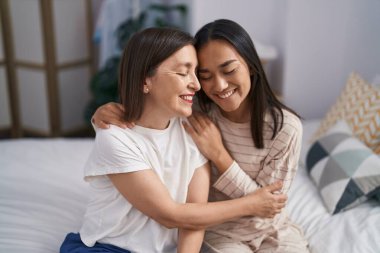 Two women mother and daughter hugging each other sitting on bed at bedroom