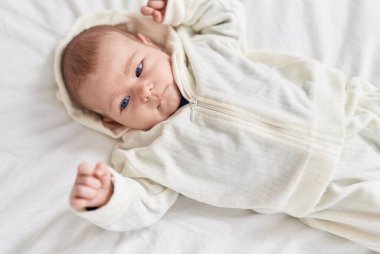 Sevimli beyaz bebek yatak odasında gevşek bir ifadeyle yatakta yatıyor.
