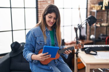 Genç İspanyol bayan müzisyen müzik stüdyosunda ukulele tutarak touchpad kullanıyor.
