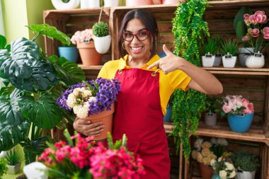 Çiçekçi dükkanında çalışan genç bir Arap kadın elinde çiçekle gülümseyen ve gururlu birini işaret ediyor. 