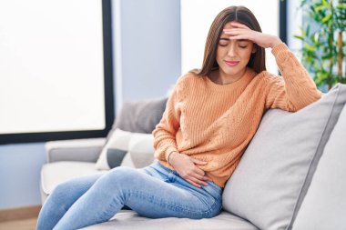 Young beautiful hispanic woman suffering for head and stomach ache at home