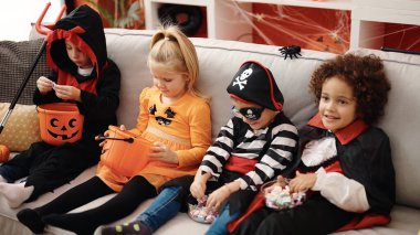 Cadılar Bayramı kostümü giyen bir grup çocuk evde şeker yiyor.