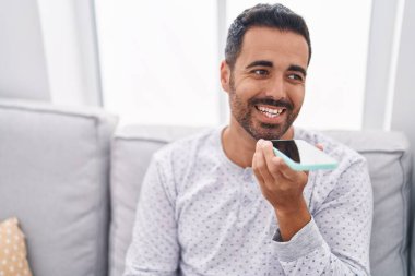 Genç İspanyol adam akıllı telefonda konuşuyor. Evdeki kanepede oturuyor.