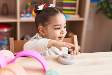Adorable hispanic girl smiling confident sitting on table at kindergarten