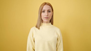 İzole edilmiş sarı arka planda gevşek bir ifadeyle duran genç sarışın kadın.