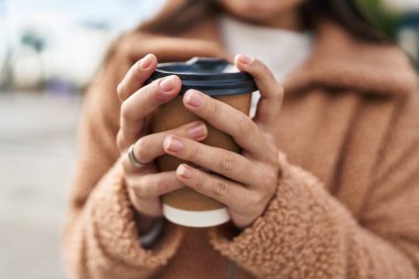 Young hispanic woman drinking coffee at street