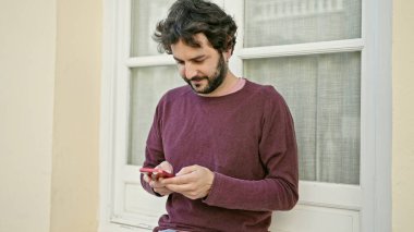 Genç İspanyol adam akıllı telefon kullanıyor. Sokakta ciddi bir ifadesi var.