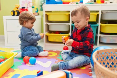Anaokulunun zemininde oturan toplarla ve inşaat bloklarıyla oynayan sevimli çocuklar.