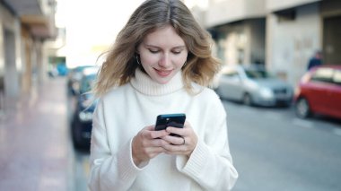 Sokakta akıllı telefon kullanan, kendine güvenen genç sarışın kadın.