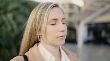 Parkta gözleri kapalı nefes alan genç sarışın kadın.