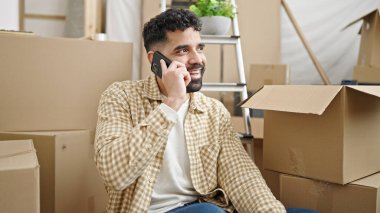 Genç İspanyol adam akıllı telefondan konuşuyor. Yeni evinde yerde oturuyor.