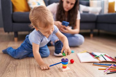 Anne ve oğlu akıllı telefon kullanarak yerde oturuyor ve evde oynuyorlar.