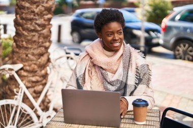 African american woman using laptop drinking coffee sitting on table at coffee shop terrace